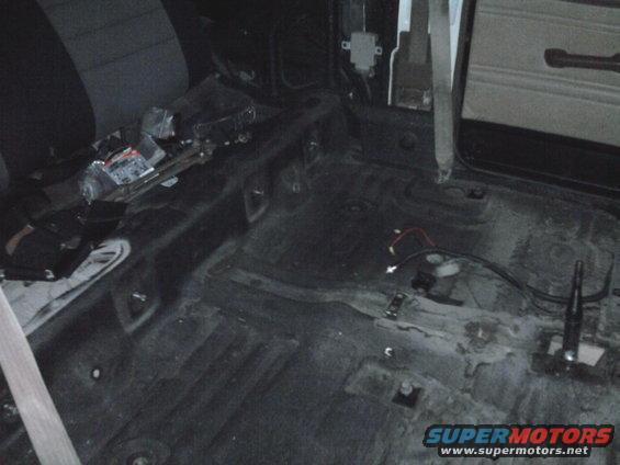 Interior of a stripped-down vehicle, showing bare floor and seats. Wires are visible