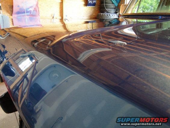 dark blue vehicle hood reflecting garage interior, tires stacked in background