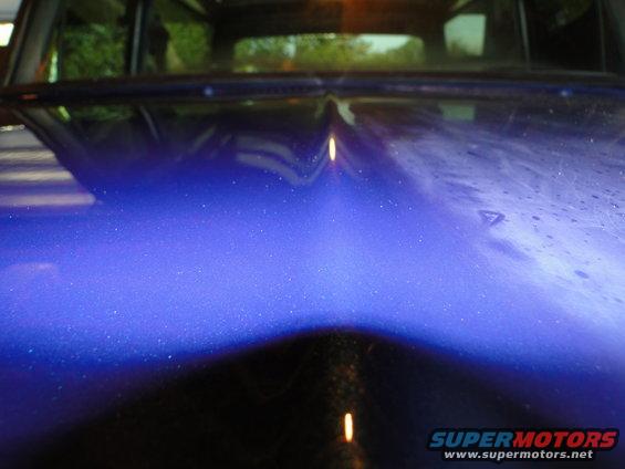 Blue metallic car hood with a central crease and reflections