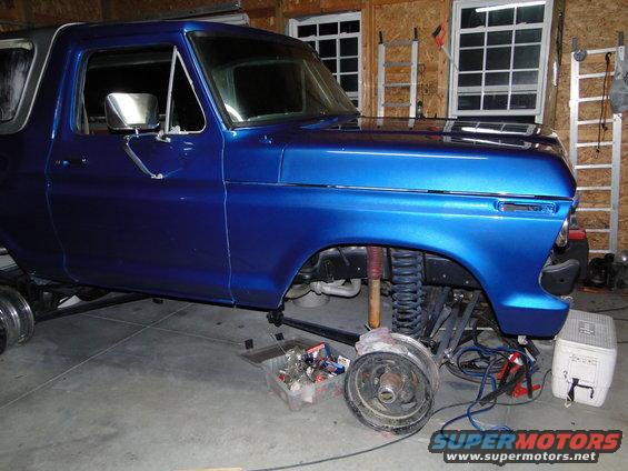 Blue 1978 Ford Bronco with front wheel removed, undergoing repairs in a garage