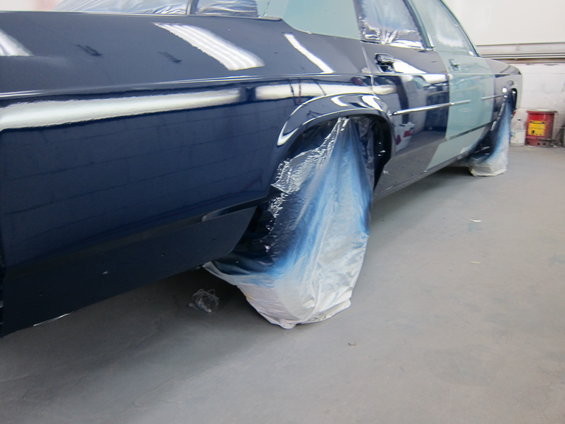 Car with blue plastic covering wheels, being prepped for paint. Rear fender and door are visible