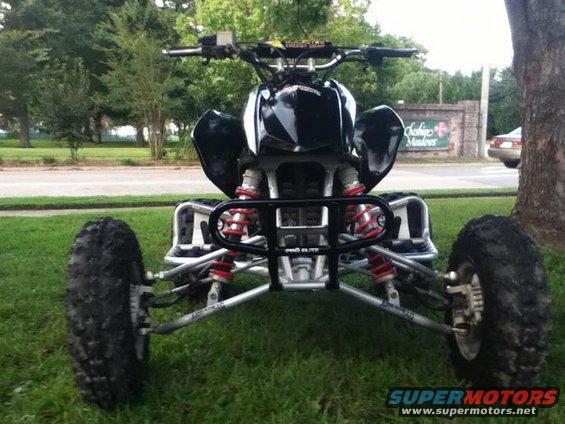 Black ATV with red suspension components and a black bumper, parked on grass