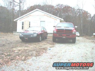 Red pickup truck parked in front of a house under construction, with a red sedan to its left