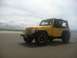 2004 Jeep TJ - Yellow Jeep TJ parked on a sandy beach under a cloudy sky.
