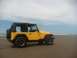 2004 Jeep TJ - A yellow Jeep TJ is parked on the sand near the ocean under a cloudy sky.