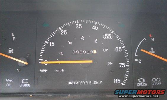 Car dashboard with speedometer, fuel gauge, temperature gauge, and warning lights. Odometer shows 0999999