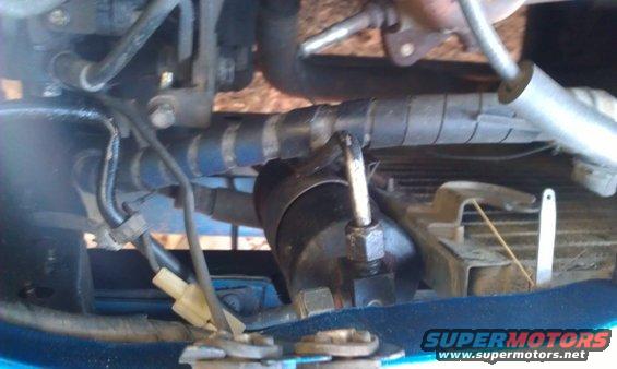 Engine bay with hoses, wires, and a black cylindrical component. Watermark reads www.supermotors.net