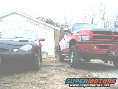 Red pickup truck parked next to a dark car in front of a garage