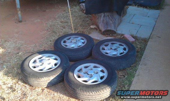 Four used tires with silver alloy wheels on the ground