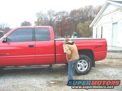 Red pickup truck with a person looking at the side panel, parked near a building