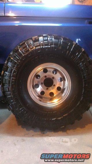 Close-up of a large, knobby off-road tire mounted on a silver multi-hole wheel, attached to the side of a blue vehicle