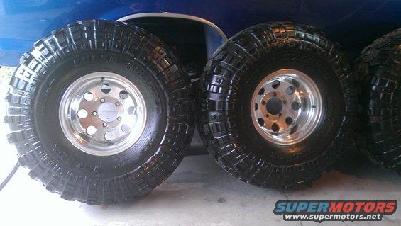 Two large off-road tires with chrome rims on a blue vehicle