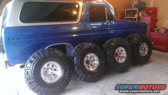 Blue SUV with a silver top, parked next to four large off-road tires