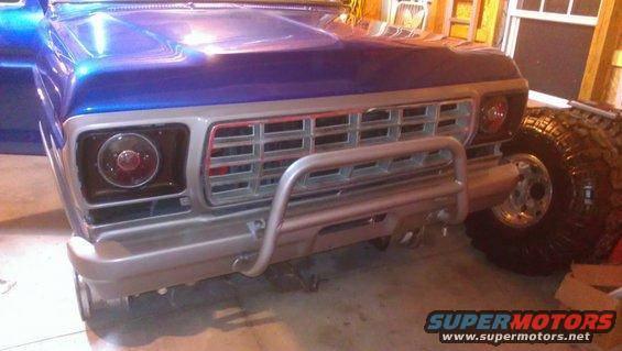 Blue 1978 Ford Bronco front end with chrome grille and brush guard. Large off-road tire visible