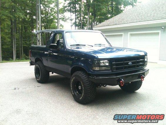 Dark blue Ford Bronco with black grille and aftermarket bumper, lifted with off-road tires