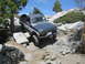 1986 Ford Bronco - This SUV is tackling a challenging off-road path with large rocks and uneven terrain.
