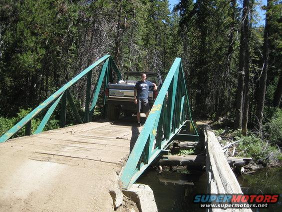 Brown Ford Bronco on a wooden bridge, driver standing next to it