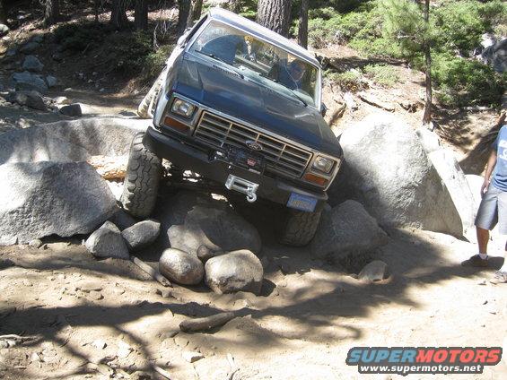 Dark blue Ford Bronco navigating large rocks on a dirt trail. Winch is mounted on the front bumper
