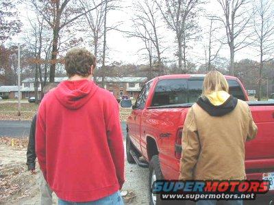 red pickup truck, rear view, two people standing nearby