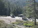 1986 Ford Bronco - Two trucks are parked on a rocky, wooded trail with people standing around them.