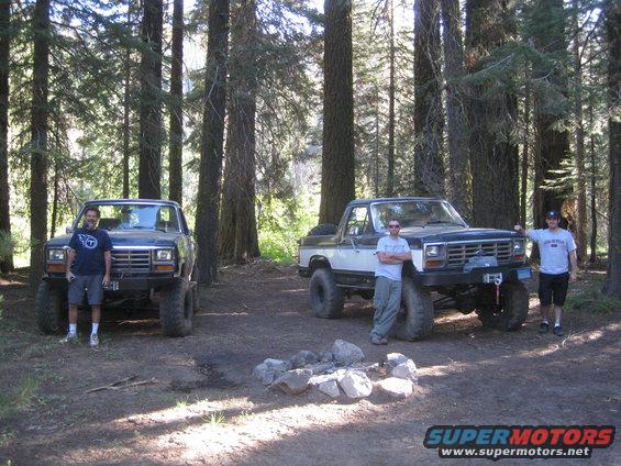 Two lifted Ford Broncos parked in a forest clearing, one black and one white/black