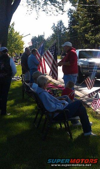 White pickup truck parked on street with American flags and people