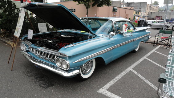 Blue 1959 Chevrolet Impala with hood open, parked on street. Another car visible in background