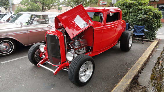 Red hot rod coupe with hood open, parked next to a tan sedan