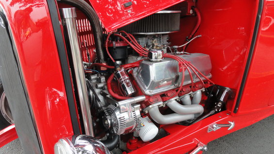 Close-up of a red hot rod's V8 engine with chrome valve covers and headers