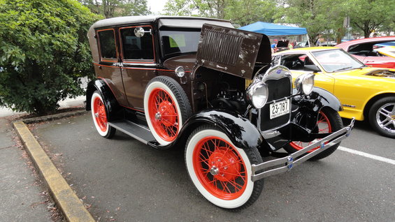 Brown sedan with red wire wheels and white sidewall tires, hood open, parked next to a yellow car