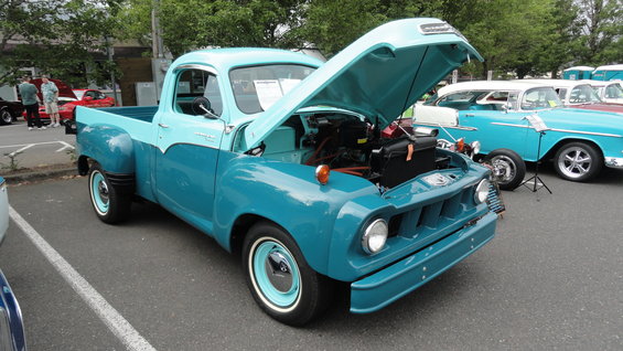 Turquoise and light blue two-tone pickup truck, hood open, parked next to a blue and white 1955 Chevrolet sedan