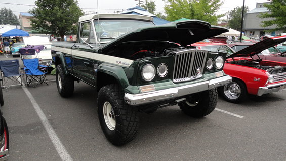 Green Jeep Gladiator pickup truck with white stripe and hood open, parked next to a red car