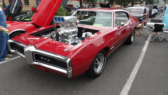 1969 Pontiac GTO with blown V8 engine, hood open. Another red car with gullwing doors is partially visible