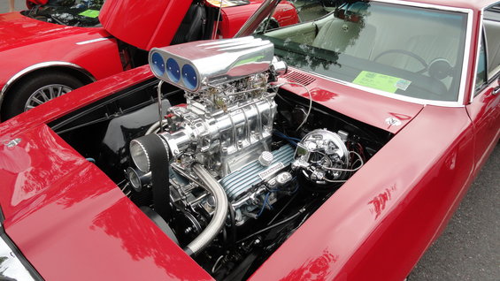 red car with hood open showing a supercharged V8 engine with chrome details