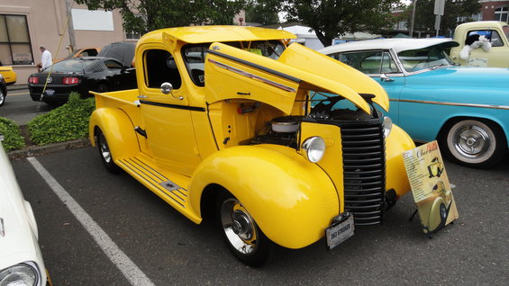 Yellow pickup truck with hood open, parked next to a blue car and a black Mustang