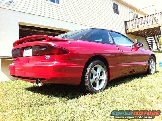 Red 1994 Ford Probe coupe, rear 3/4 view, parked on grass next to a house