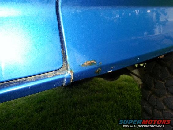 Blue vehicle lower body panel showing rust near the wheel well