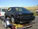 1987 Ford Mustang - A black 1987 Ford Mustang is being transported on a trailer, showing its rear end with missing components.