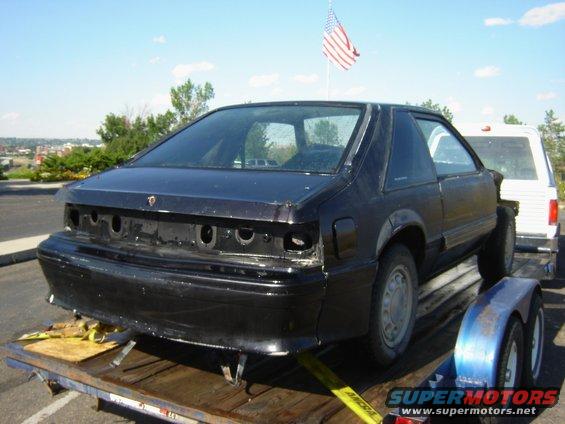 Black 1987 Ford Mustang coupe on a trailer, rear view, missing taillights and bumper