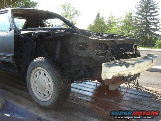 1987 Ford Mustang chassis with front bumper removed, on a flatbed trailer