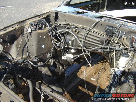 1987 Ford Mustang engine bay with exposed wiring and wooden floor