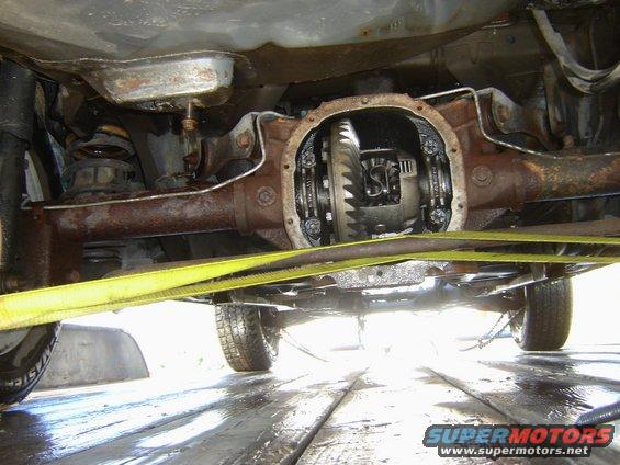 Underside view of a vehicle's rear differential, partially disassembled. Yellow straps are visible
