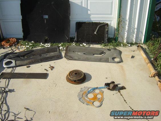 Car parts laid out on concrete, including door panels, radiator, and driveshaft