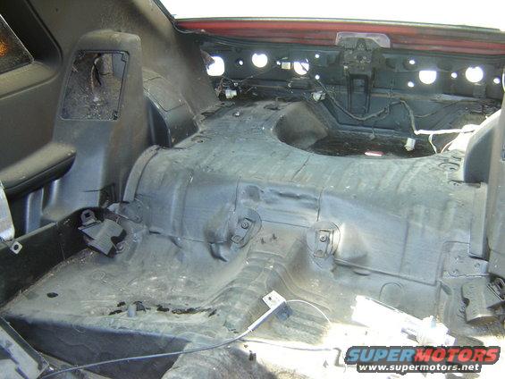 Stripped interior of a 1987 Ford Mustang trunk area, showing exposed metal and wiring