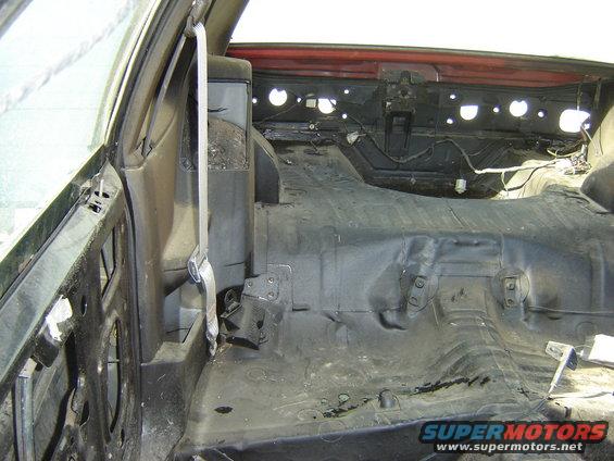 Car interior stripped down, showing floor pan and seat belt anchor points