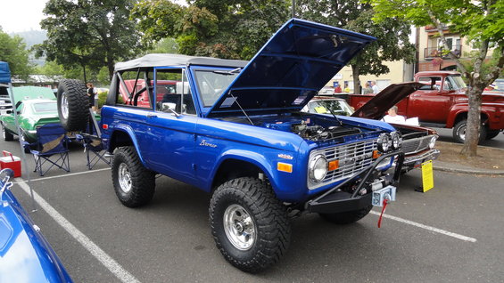 Blue Ford Bronco with hood open, spare tire mounted on rear, off-road tires, aftermarket bumper with winch