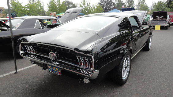 Black 1967 Ford Mustang fastback with chrome wheels, seen from rear quarter angle