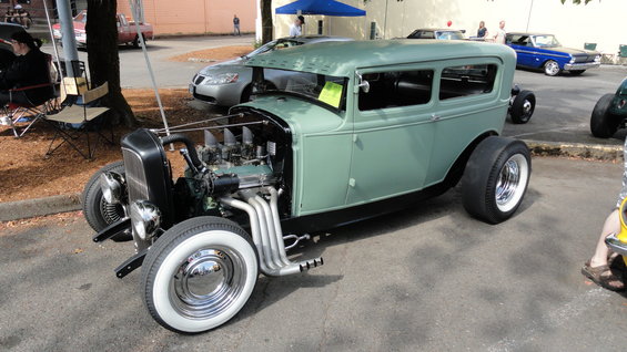 Green hot rod sedan with exposed engine, whitewall tires, and chrome exhaust pipes