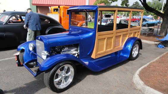blue woody wagon hot rod with chrome wheels and exposed engine, parked next to a black car