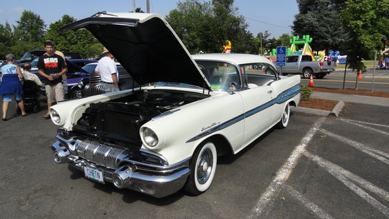 White 1957 Pontiac Bonneville with blue side trim, hood open, parked at an outdoor event